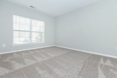 an empty living room with a window and carpet