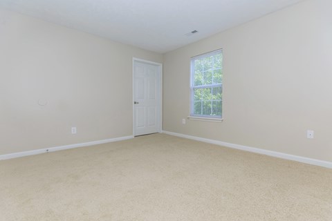 A room with a carpeted floor, a door, and a window with blinds.
