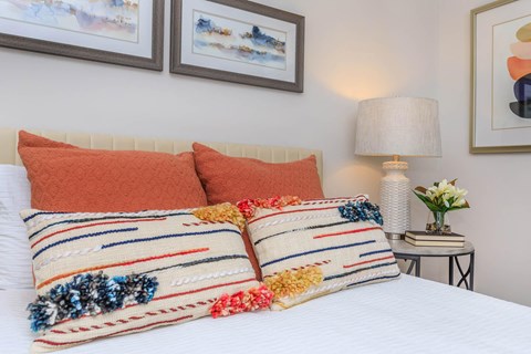 A bed with two striped pillows and a flower vase on a side table.