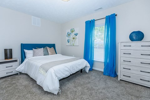A bedroom with a white bed and blue curtains.
