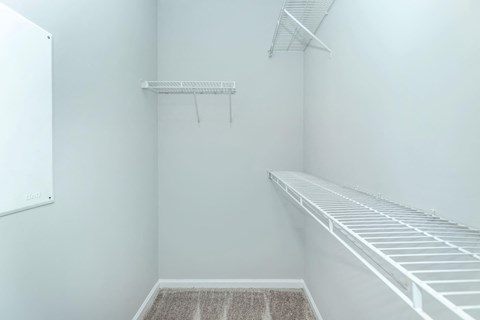 a walk in closet with white walls and shelves and a wire rack on the wall