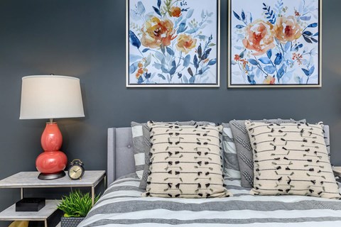 A bedroom with a bed, pillows, a lamp, and two floral paintings on the wall.