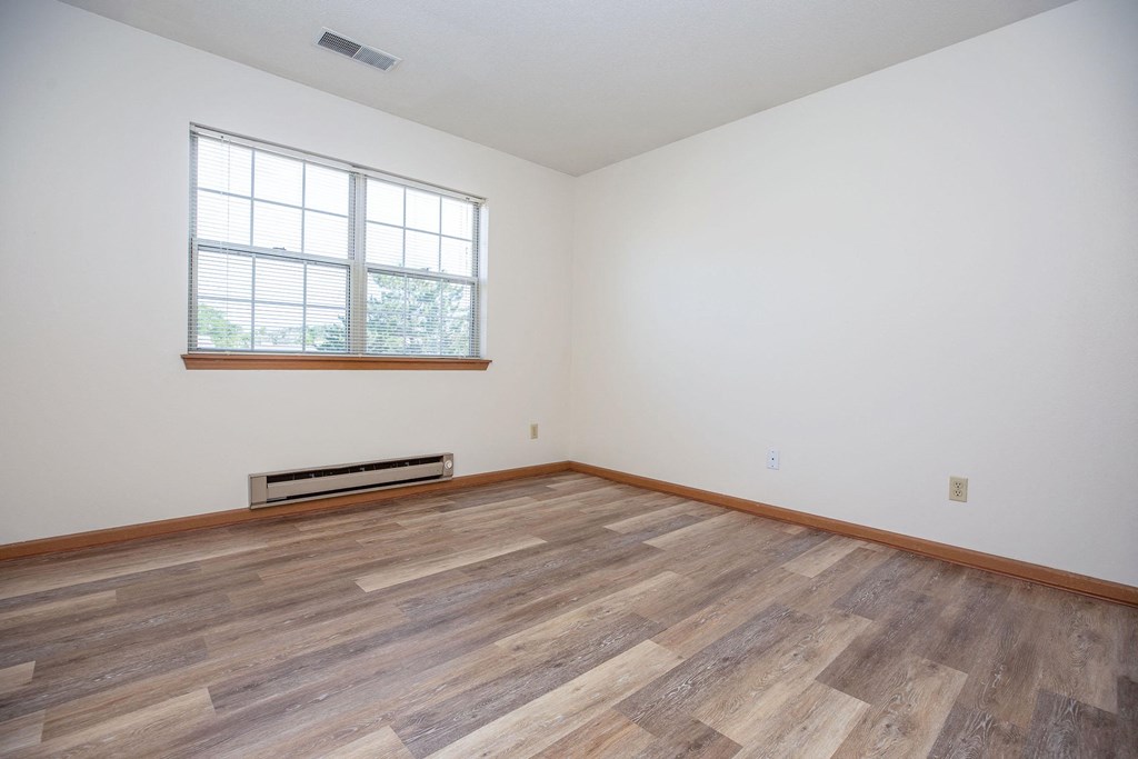 the living room of an empty house with wood flooring and a window