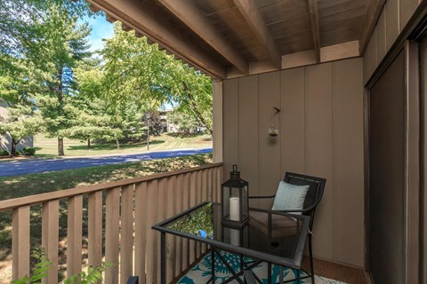 a balcony with a glass table and chairs and a view of a park