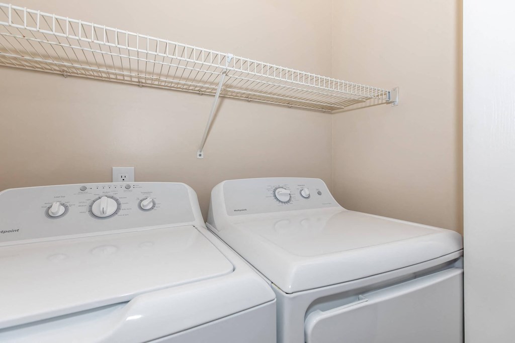 two washers and dryers in a laundry room with a shelf above them
