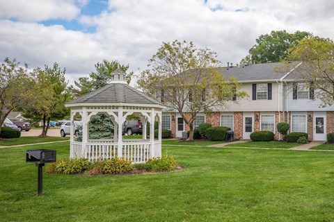 A white gazebo is in the middle of a grassy area in front of a house.