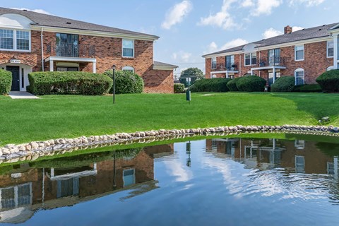 a pond in front of a house with a yard and a building