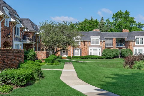 an exterior view of an apartment complex with a green lawn and sidewalk