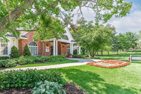 the front yard of a brick house with a garden and trees