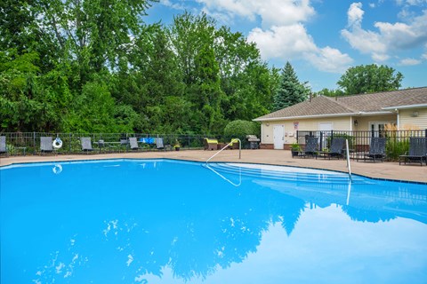 A large blue swimming pool surrounded by trees and a house.