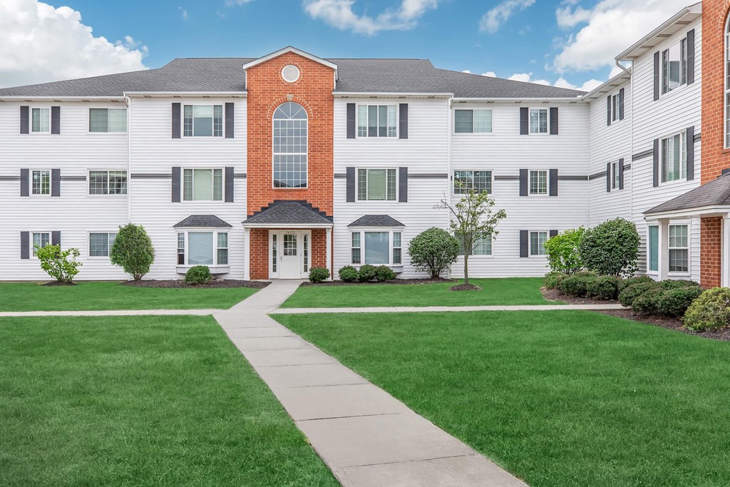a large white apartment building with green grass and a sidewalk