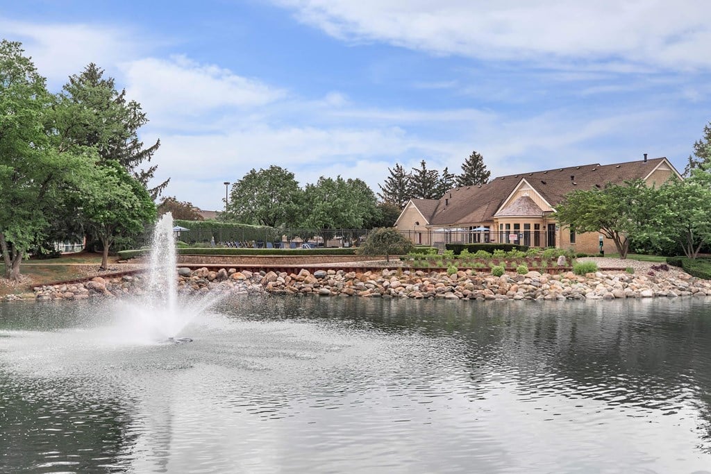 a fountain in the pond with a house in the background