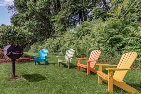 A set of four colorful chairs are arranged in a row on a lawn.
