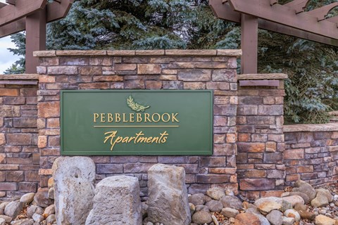 A sign that says Pebblebrook Apartments in front of a stone wall.