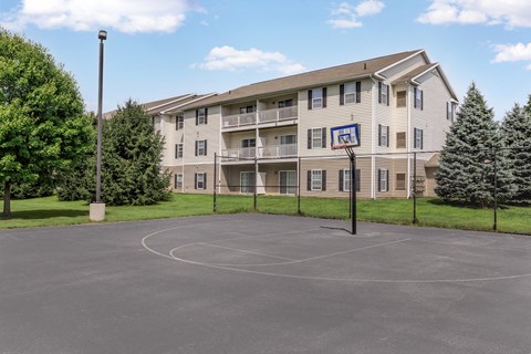 A basketball court is in the foreground of a large apartment complex.