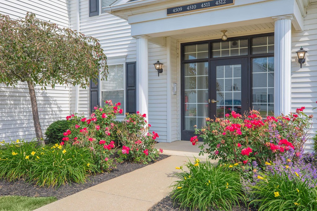 the front of a house with a sidewalk and colorful flowers