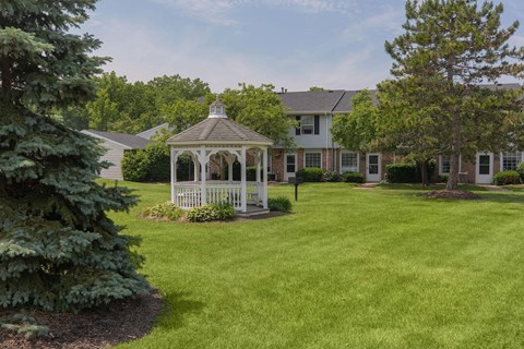 A gazebo is in the middle of a grassy area in front of a house.