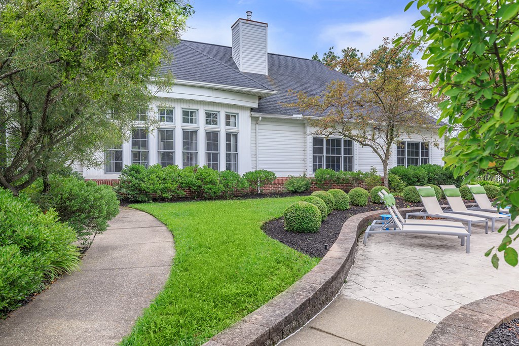 a walkway leading to a house with chairs and a garden