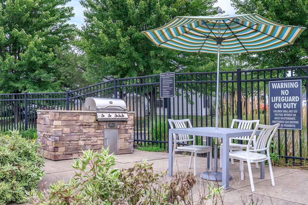 a patio with an umbrella and a table with chairs and a grill