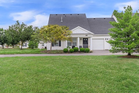 the front of a white house with a lawn and trees