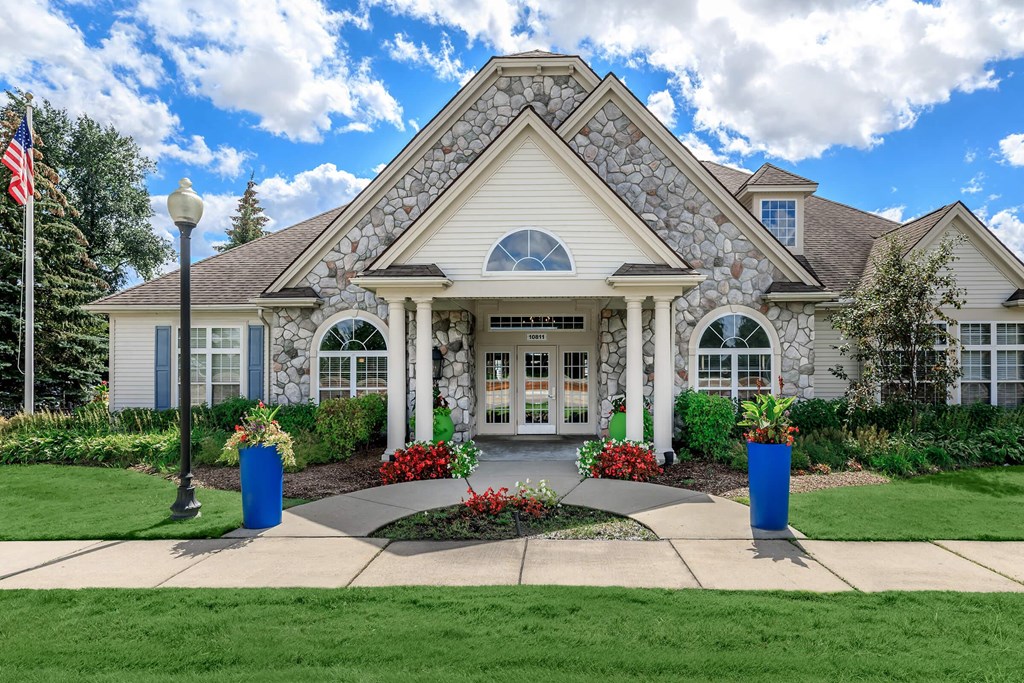 the front of a house with flowers and a flag on the sidewalk
