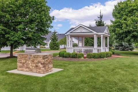 a gazebo in the middle of a lawn with trees and a statue