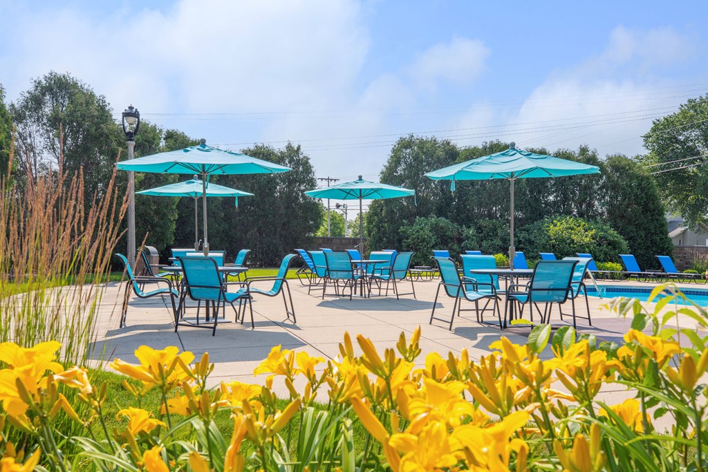a patio with blue chairs and umbrellas and yellow flowers