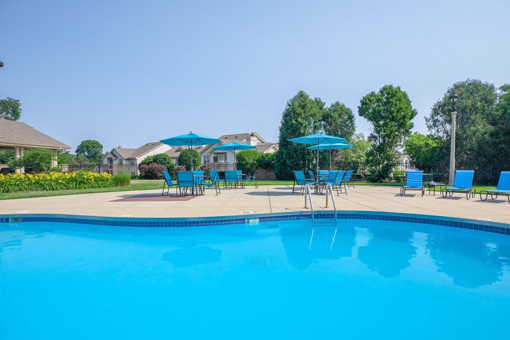 a swimming pool with blue chairs and umbrellas next to a resort style pool