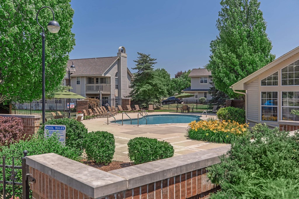 a swimming pool in front of a house with a patio and trees