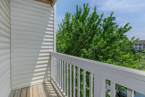 A white balcony with a wooden floor and a tree in the background.