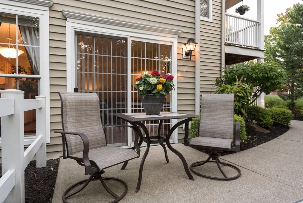 A patio with a table and two chairs with a pot of flowers on the table.