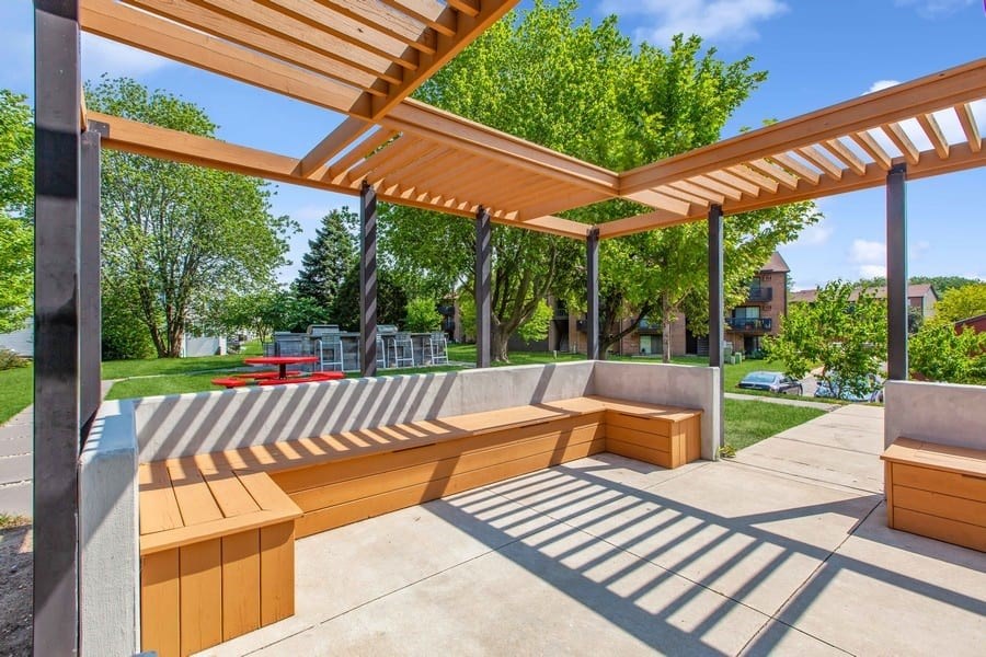 A wooden bench under a wooden pergola on a sunny day.