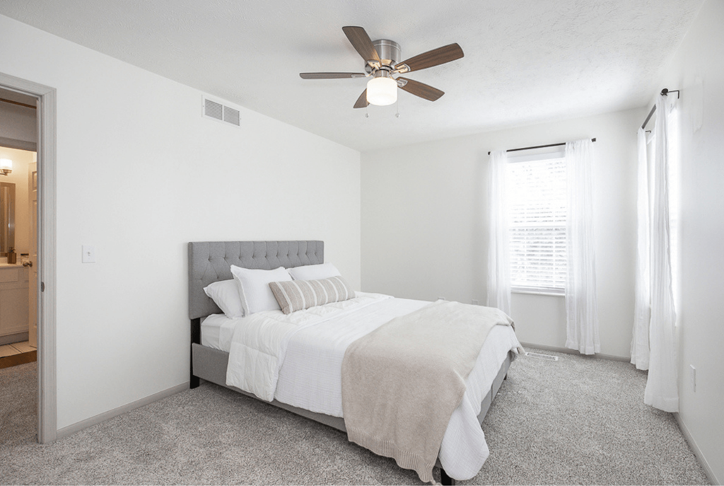 A bedroom with a bed, carpet, and a ceiling fan.