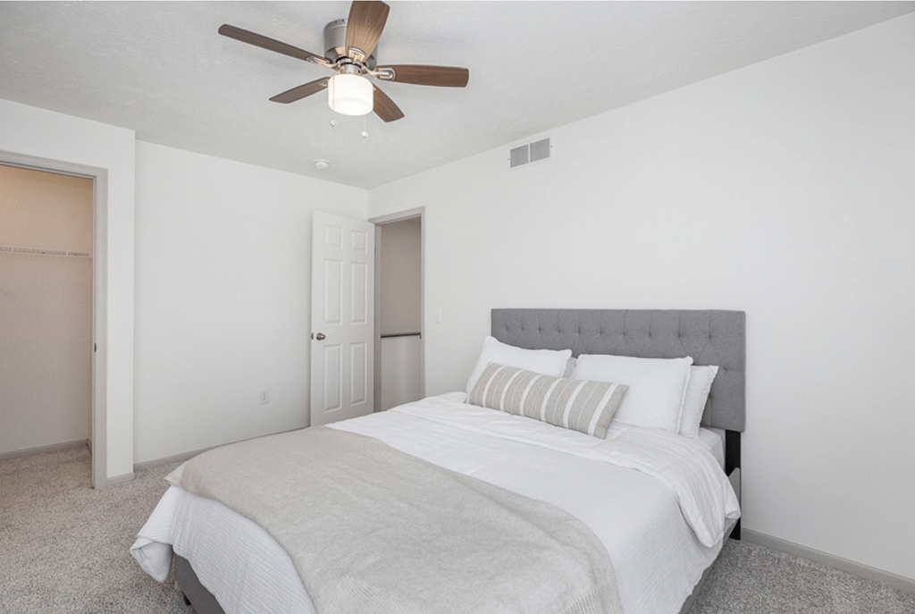 A bedroom with a bed, pillows, and a ceiling fan.