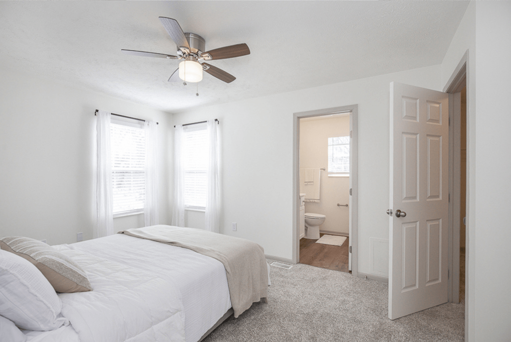 A bedroom with a bed, a ceiling fan, and a bathroom visible through the door.