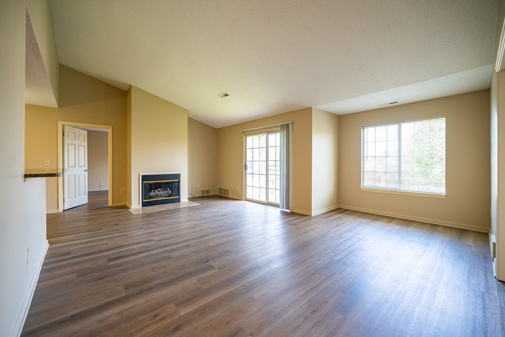 Living room without furniture, gas fireplace, plank foor and windows along right wall