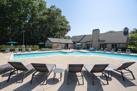 A pool surrounded by chairs and umbrellas with a building in the background.