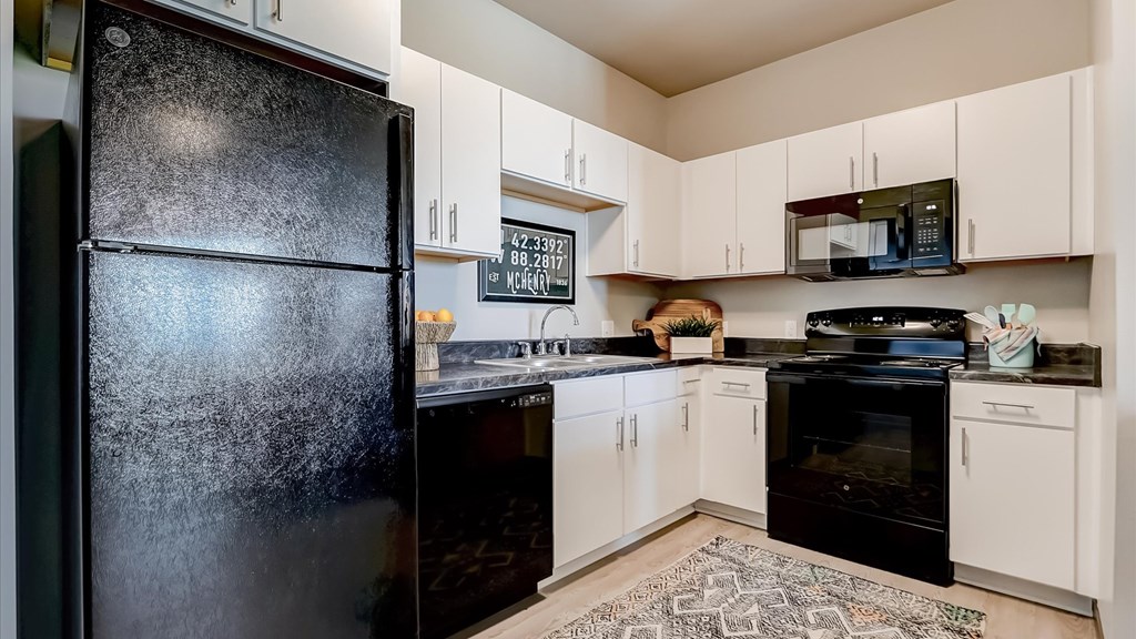 A black refrigerator in a kitchen with white cabinets.