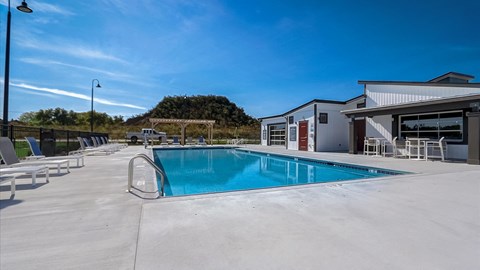 A large outdoor swimming pool with lounge chairs and a building in the background.