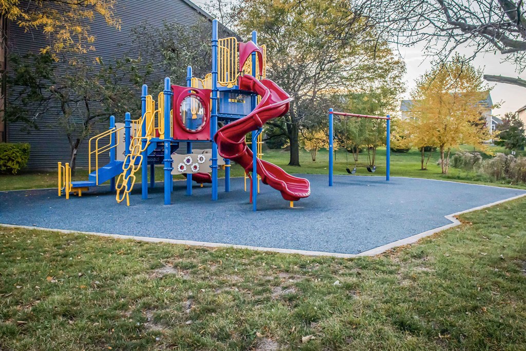 A playground with a red slide and yellow handrails.