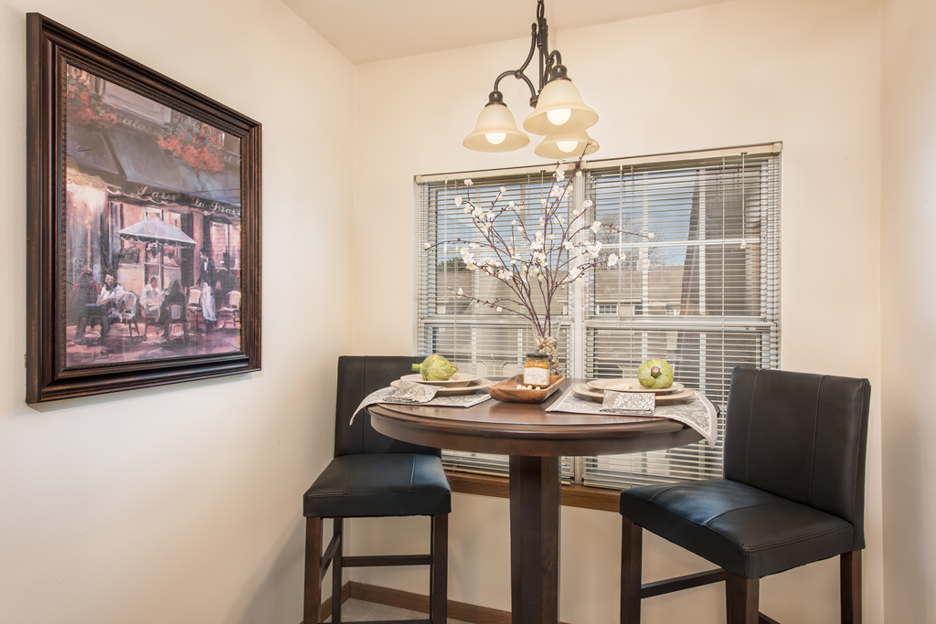 a dining area with a table and chairs and a window with blinds