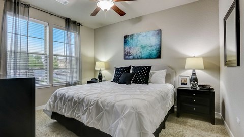 A bedroom with a large bed, a ceiling fan, and a painting on the wall.