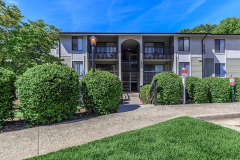 a sidewalk in front of an apartment building with manicured bushes