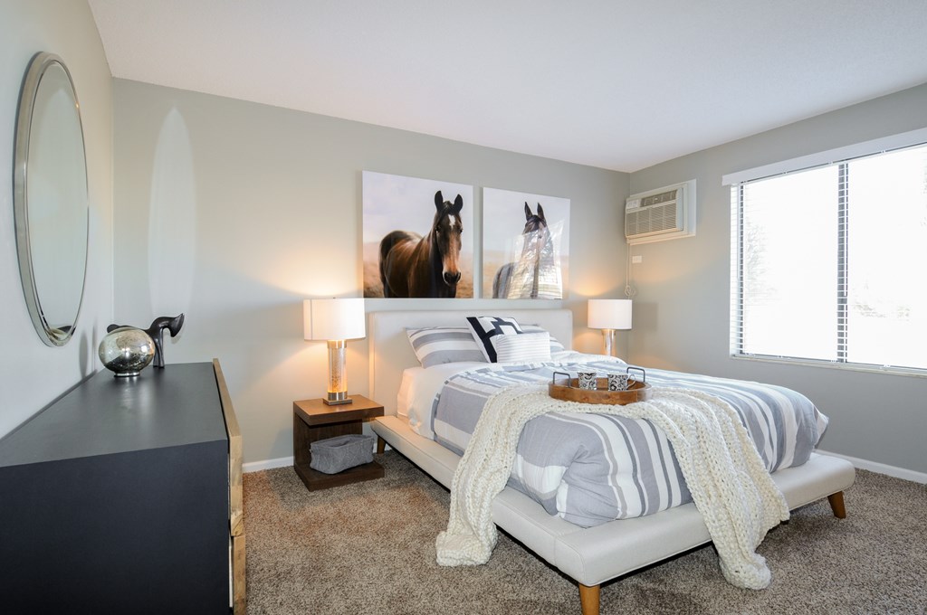 A bedroom with a bed, nightstand, and a large picture of a horse on the wall.