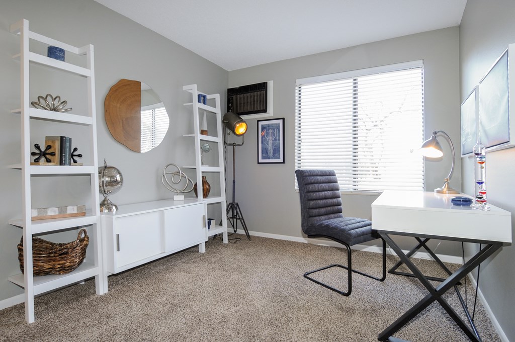 A room with a white desk, a black chair, and a white shelf with various objects on it.