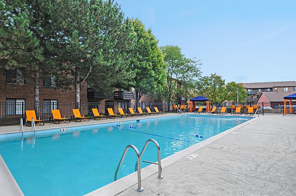 A pool with orange chairs and trees in the background.
