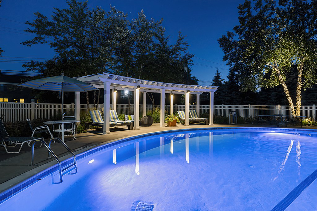 a swimming pool at night with a pavilion and chairs around it