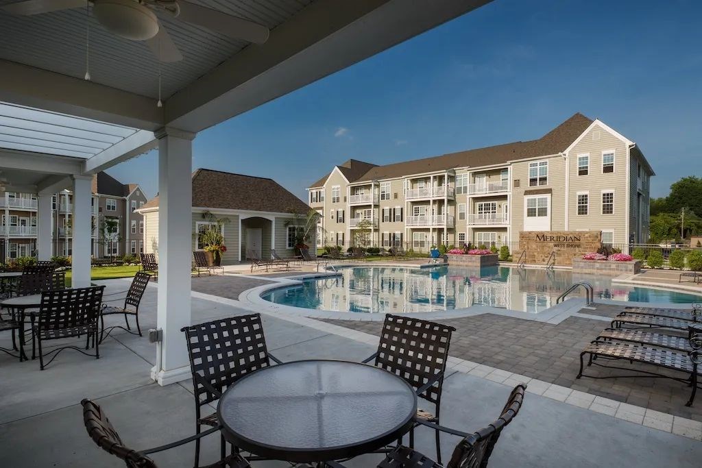 A pool area with chairs and a table in front of apartment buildings.at Meridian West Shore, Pennsylvania 17055