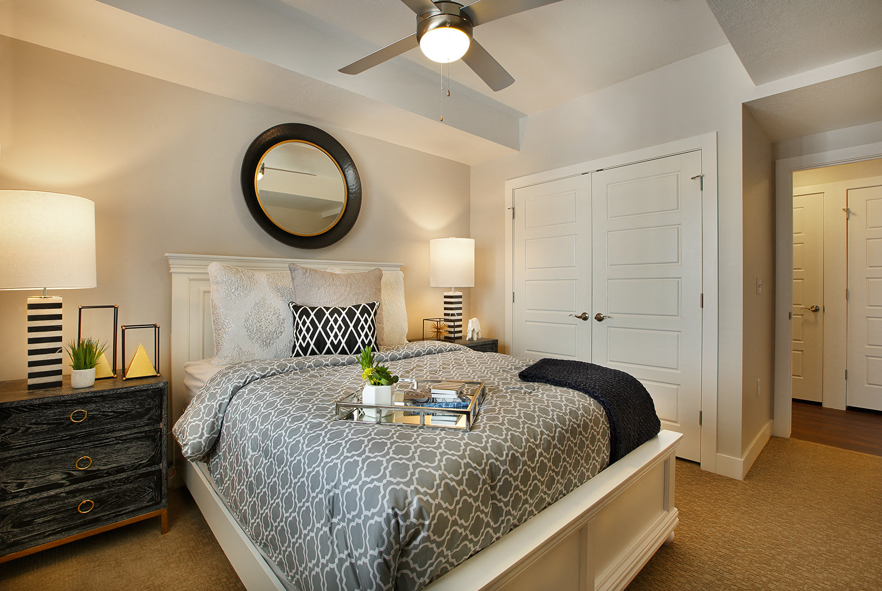 A bedroom with a patterned bedspread and a round mirror on the wall.