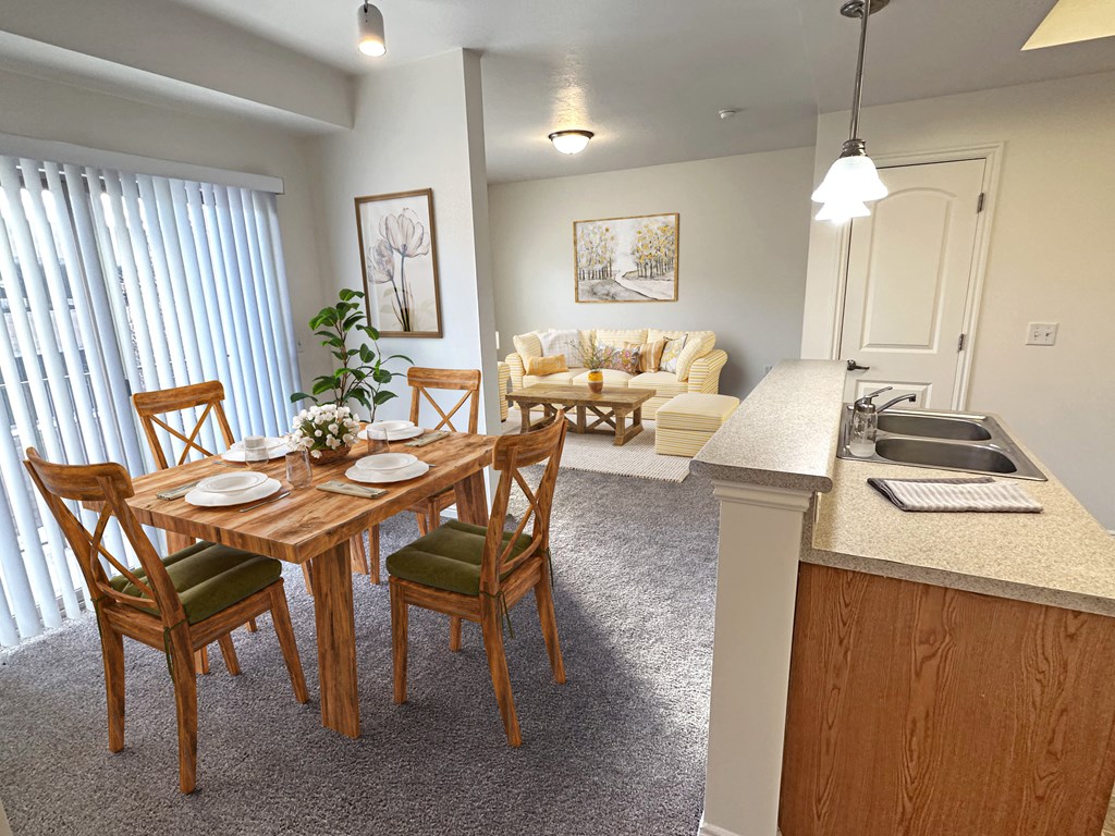 Liberty Landing Apartments in West Jordan Utah living room in Lambert floor plan with four-seat dining table in front of sink and living room in the background.
